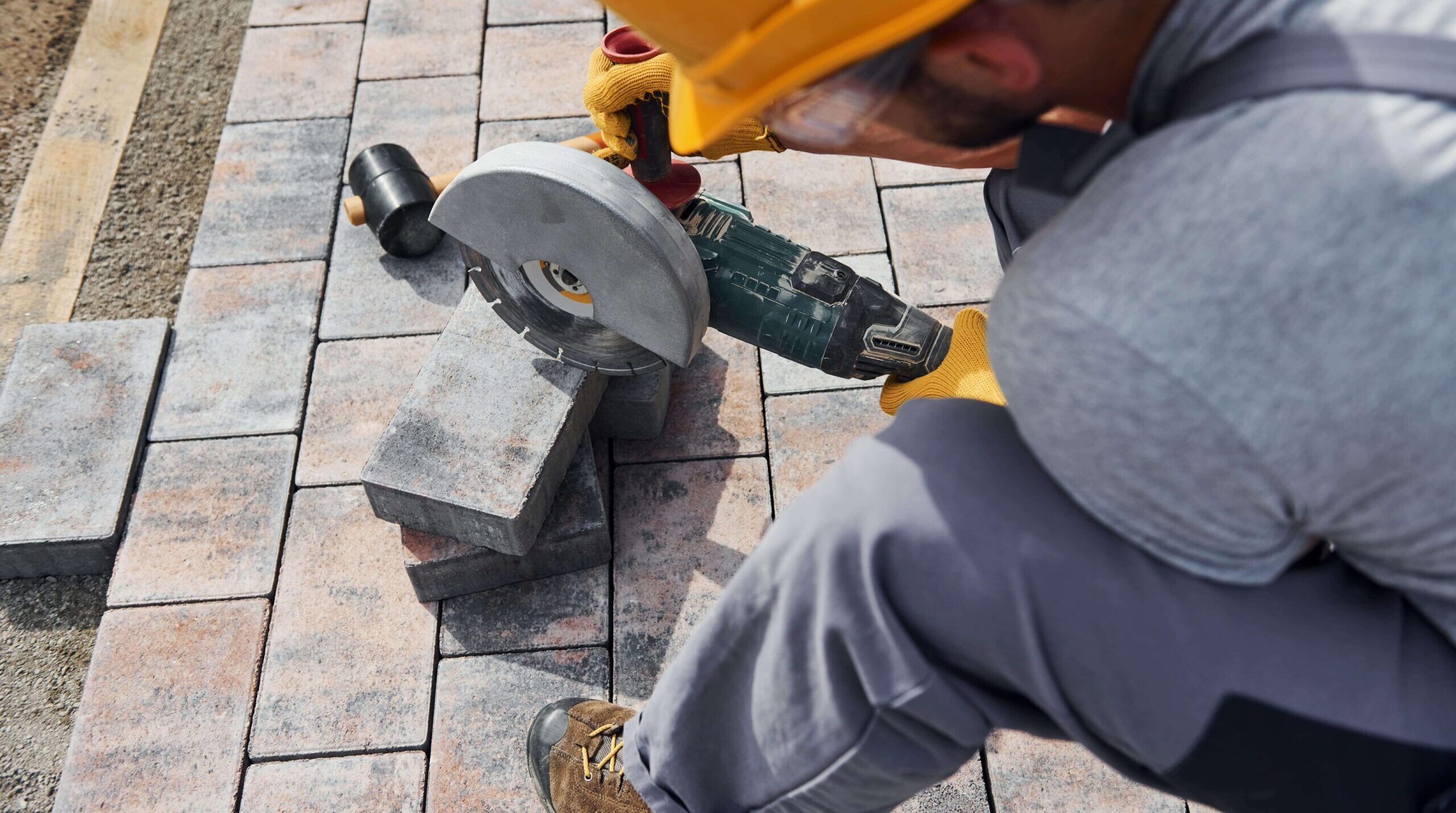 Patio builder using a power tool to cut a patio paver